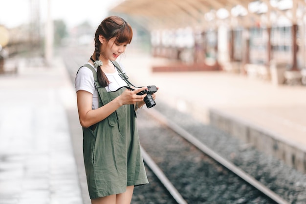 Ritratto giovane donna asiatica sorridente turista Viaggiatore ragazza a piedi e con una tenuta la fotocamera attende viaggio in treno viaggio è preso in piattaforma ferroviaria Thailandia estate relax vacanza Concept