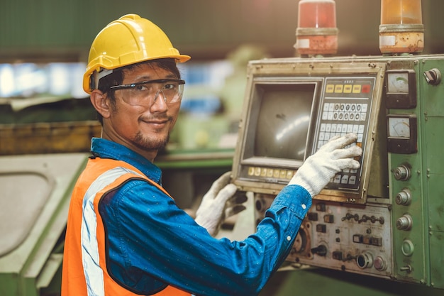 Ritratto Il lavoratore asiatico felice aziona la macchina CNC nel personale della fabbrica dell'industria siderurgica pesante che sorride con il pannello di controllo meccanico