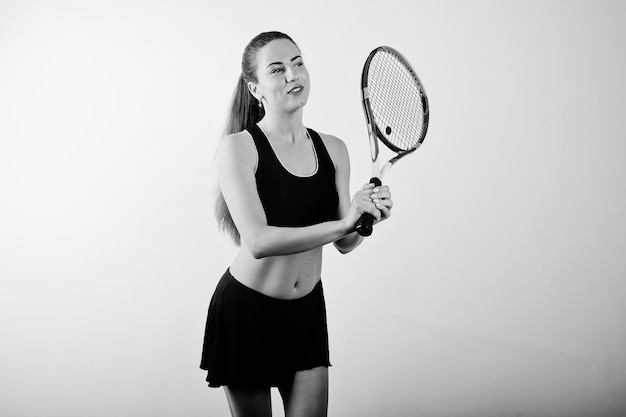 Ritratto in bianco e nero di una bella giovane donna in abiti sportivi che tiene una racchetta da tennis mentre si trova su uno sfondo bianco