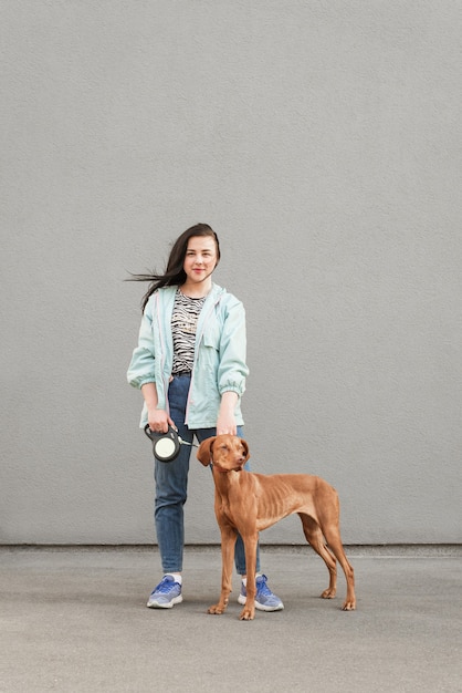 Ritratto in piena altezza ragazza positiva con un bellissimo cane marrone al guinzaglio