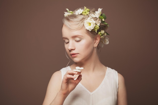 Ritratto in primo piano del viso di bellezza di una signora fresca ed elegante con la pelle pulita e sana che indossa fiori bianchi di primavera