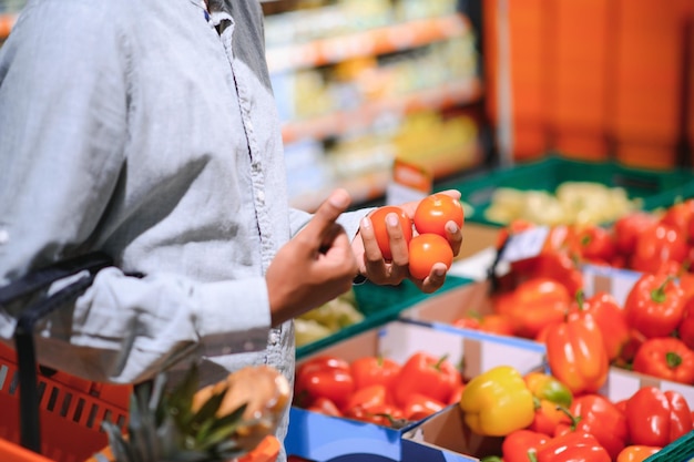 Ritratto in primo piano di un bel giovane che raccoglie peperoncini scegliendo verdure gialle e arancioni al supermercato