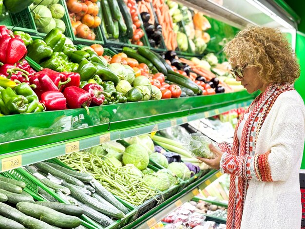 Ritratto in primo piano di una bella giovane donna in maglione che sceglie verdure a foglia verde al negozio di alimentari