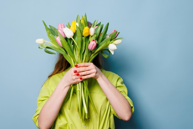 ritratto in primo piano di una donna con un bouquet di fiori di tulipano su uno sfondo blu pulito congratulazioni concetto