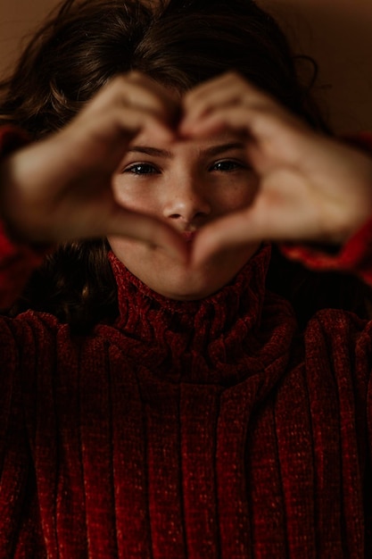 Ritratto in primo piano di una ragazza che fa la forma di un cuore su uno sfondo marrone