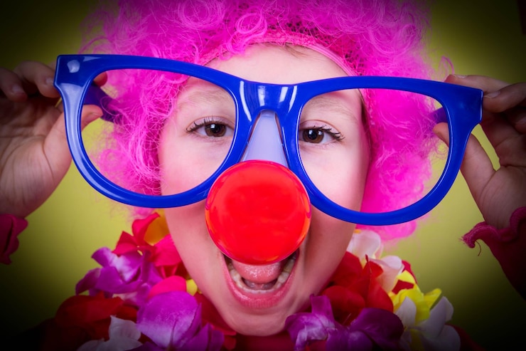 Foto ritratto in primo piano di una ragazza che indossa un naso da clown e occhiali da sole su uno sfondo giallo