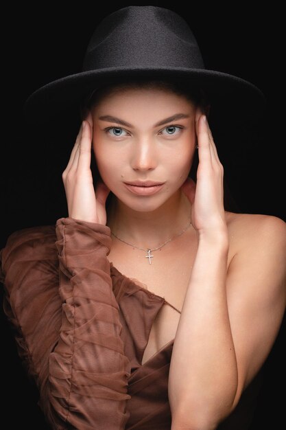 Ritratto in studio alla moda di una bella ragazza con cappello nero su sfondo nero