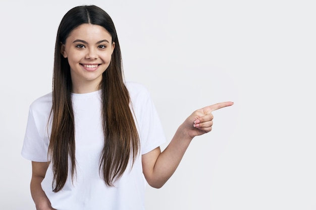 Ritratto in studio del primo piano di una bella ragazza adolescente dai capelli castani sorridente guardando la fotocamera indossando maglietta bianca isolata su sfondo bianco mostrando lo spazio della copia per il testo pubblicitario Mockup