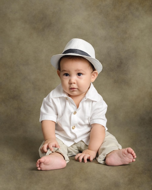 Ritratto in studio di bambino sorridente che indossa il cappello bianco seduto sul pavimento