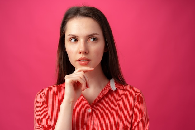 Ritratto in studio di bella giovane donna che pensa su sfondo rosa