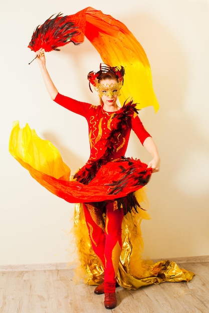 Ritratto in studio di donna in movimento che esegue la sua danza esotica Graziosa ragazza in costume rosso che tiene i fan con lunghi veli rossi e gialli Costume luminoso come parte dell'immagine