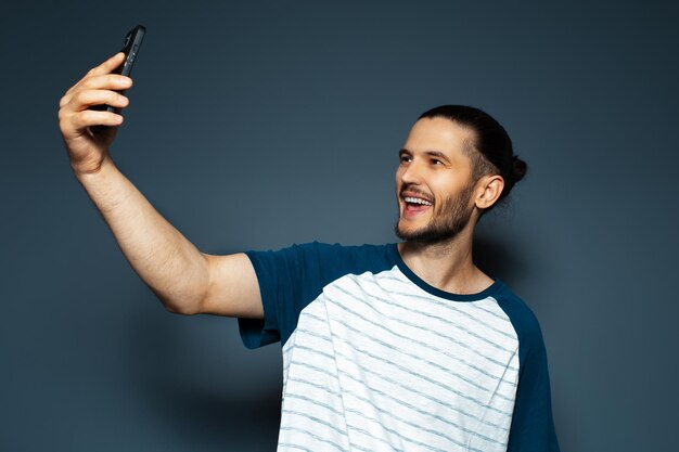 Ritratto in studio di giovane bel ragazzo sorridente che prende selfie con lo smartphone