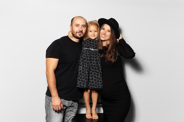 Ritratto in studio di giovane famiglia felice su sfondo bianco Indossare il cappello vestito di nero Figlia che abbraccia i suoi genitori