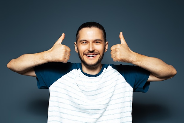 Ritratto in studio di giovane uomo che mostra i pollici in su su sfondo di colore blu