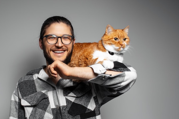 Ritratto in studio di giovane uomo felice con gatto rosso su sfondo grigio