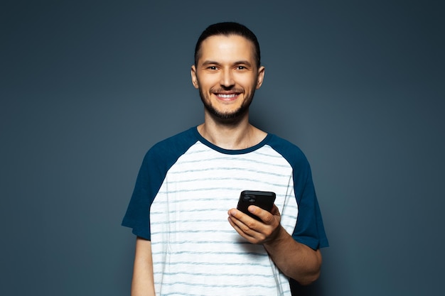 Ritratto in studio di giovane uomo sorridente in possesso di uno smartphone