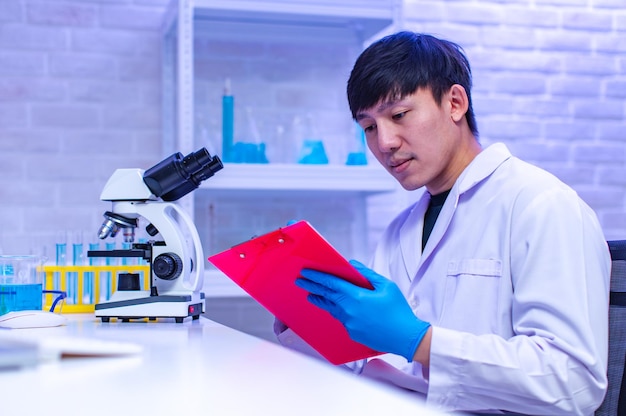 Ritratto in studio di scienziato maschio professionista asiatico in guanti di gomma da laboratorio bianco seduto sorridente sguardo alla fotocamera che mostra la provetta del campione nelle mani nella sala di lavoro del laboratorio dell'ospedale.