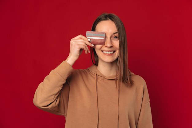 Ritratto in studio di un'ampia donna sorridente che copre l'occhio con una carta di credito rossa