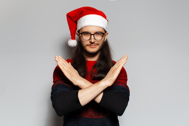 Ritratto in studio di un bel ragazzo sorridente che mostra il gesto No o Stop con le mani Indossando il cappello di Babbo Natale Concetto di Natale Sfondo bianco