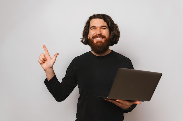 Ritratto in studio di un giovane che punta verso l'alto tenendo il portatile aperto