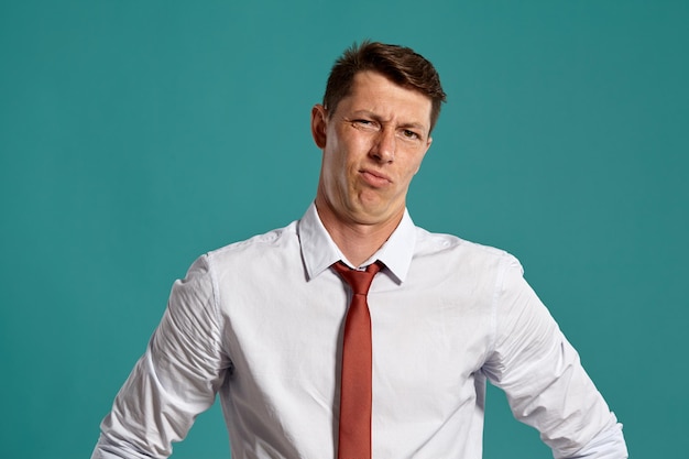 Ritratto in studio di un giovane lunatico in una classica camicia bianca e cravatta rossa che sembra sconvolto mentre posa su uno sfondo blu. Taglio di capelli alla moda. Concetto di emozioni sincere. Copia spazio.