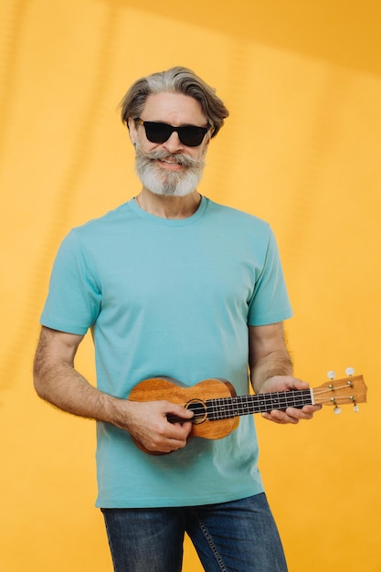 Ritratto in studio di un uomo anziano in occhiali da sole che suona un ukulele