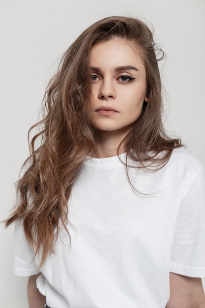 Ritratto in studio di una bella ragazza con i capelli in una maglietta bianca alla moda su sfondo bianco