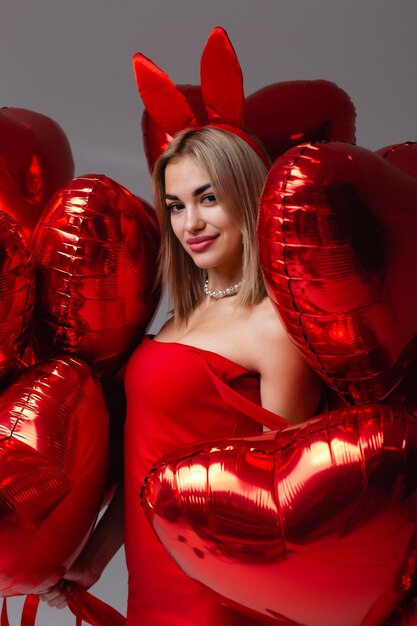Ritratto in studio di una bella ragazza sorridente in un vestito rosso Modello in posa con palloncini a forma di cuore