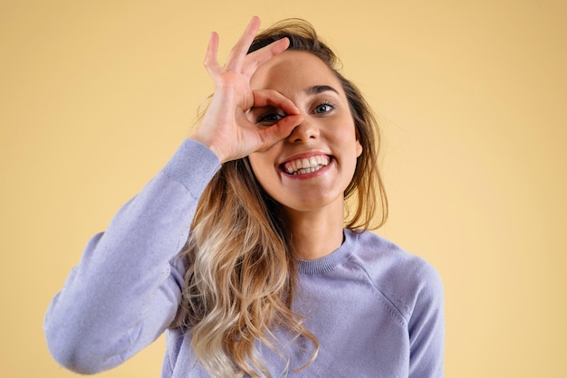 Ritratto in studio di una donna attraente che mostra un gesto okey isolato su sfondo giallo