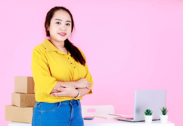 Ritratto in studio di una donna d'affari asiatica felice professionale di successo giovane imprenditrice di avvio femminile in piedi con le braccia incrociate sorridente guarda la telecamera alla reception con spedizione su sfondo rosa.