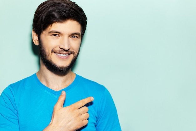 Ritratto in studio di uomo sorridente, mostrando con il dito sullo spazio vuoto di sfondo blu.