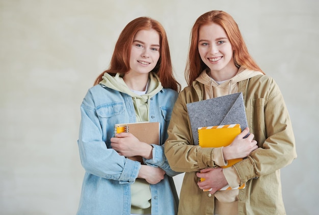 Ritratto in studio medio orizzontale di due studenti universitari gemelli moderni che indossano abiti casual in possesso di libri di testo sorridenti alla telecamera