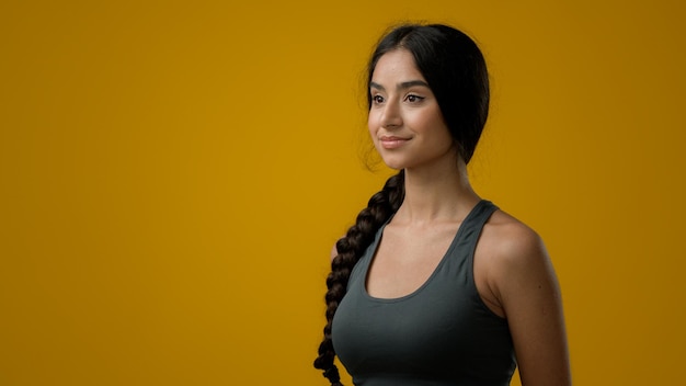 Ritratto in studio sportivo 20s donna etnica indiana capelli lunghi in posa in piedi su sfondo giallo
