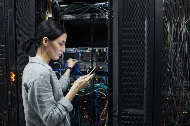 Ritratto in vista laterale del tecnico di rete femminile che collega i cavi nell'armadio del server durante la configurazione del supercomputer nel data center, copia dello spazio