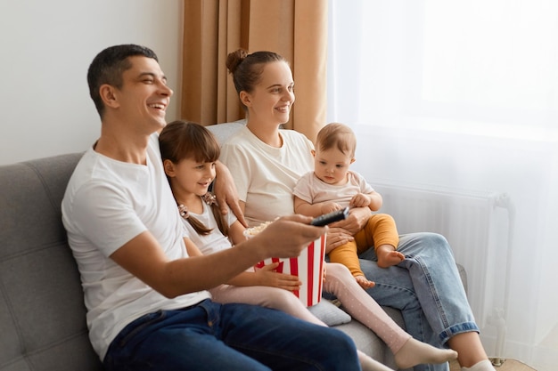 Ritratto in vista laterale della famiglia seduta sul divano con telecomando e guardando la tv godendo di film o cartoni interessanti che sono estremamente felici di stare insieme a casa