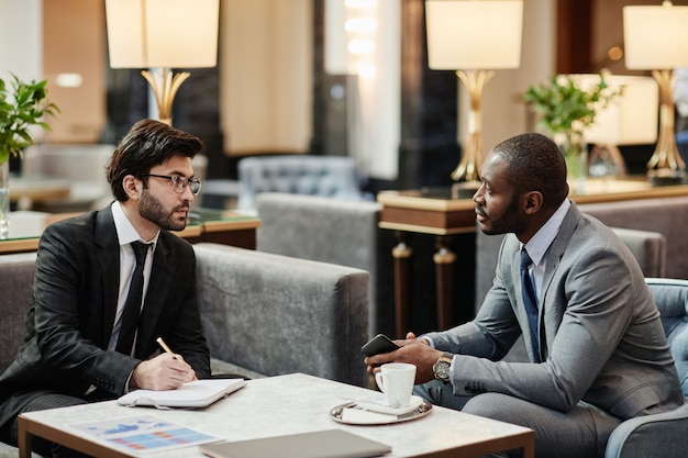 Ritratto in vista laterale di due partner commerciali che discutono di un accordo nella lussuosa hall dell'hotel, copia spazio