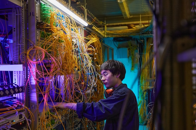 Ritratto in vista laterale di un giovane tecnico di rete che collega i cavi nella sala server, copia spazio