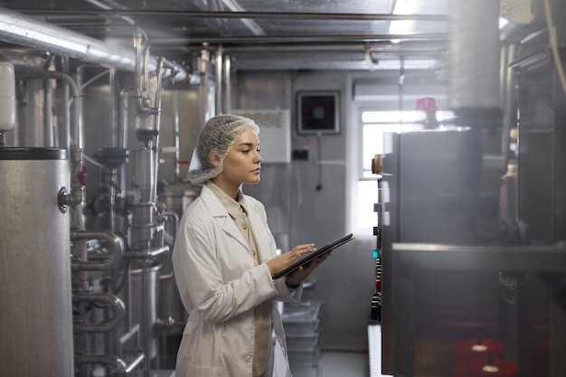 Ritratto in vista laterale di una lavoratrice che tiene in mano un tablet digitale durante l'ispezione del controllo di qualità presso l'officina della fabbrica di alimenti, spazio di copia