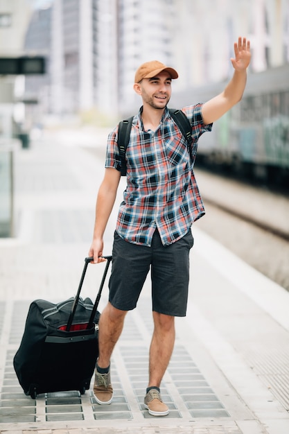 Ritratto in vita di un bell'uomo che alza la mano distogliendo lo sguardo e sorride alla stazione ferroviaria