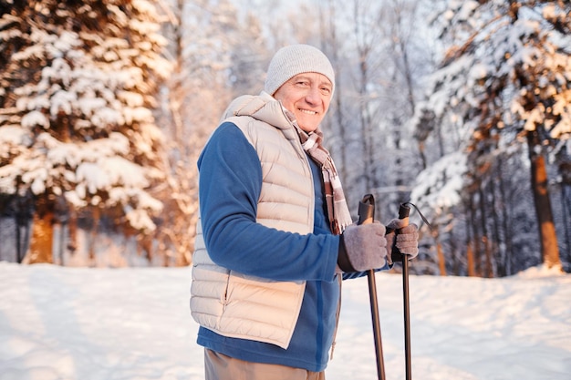 Ritratto in vita di un uomo maturo sorridente che si gode la passeggiata nordica nella foresta invernale allo spazio della copia del tramonto