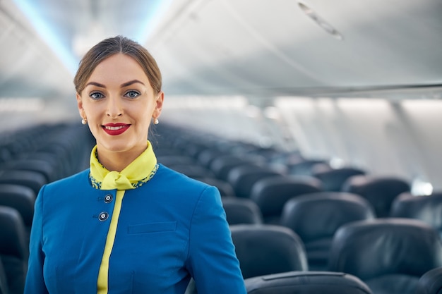 Ritratto in vita di una donna allegra felice che indossa l'uniforme blu dell'assistente di volo con guanti di pelle gialla in posa davanti alla telecamera sulla scheda vuota