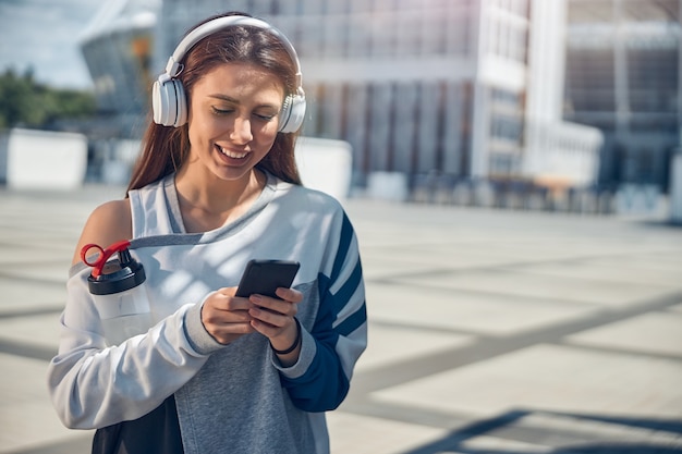 Ritratto in vita di una donna sportiva e vivace che fissa il suo telefono cellulare nelle sue mani