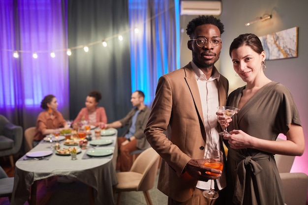 Ritratto in vita di una giovane coppia di razza mista che guarda l'obbiettivo durante la cena con gli amici, copia spazio