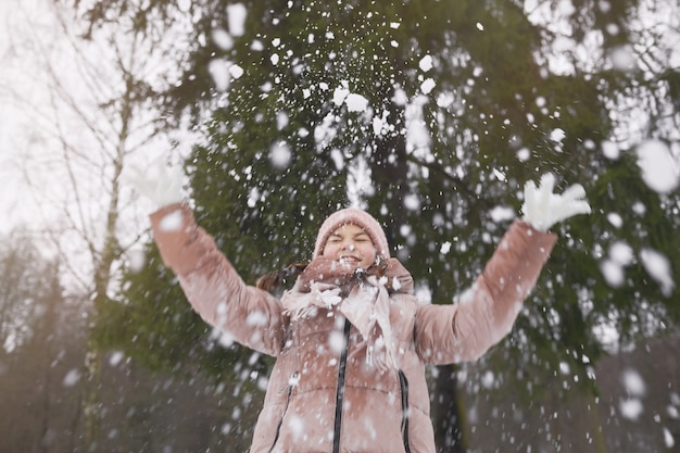 Ritratto in vita di una ragazza allegra felice che lancia la neve mentre si gode una passeggiata nella foresta invernale all'aperto, copia spazio