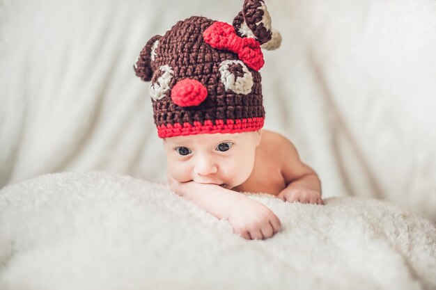 Ritratto infantile sorridente felice del neonato vestito in cappello lavorato all'uncinetto dei cervi di natale, concetto di vacanze invernali