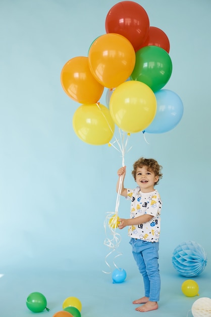 Ritratto integrale del ragazzo allegro che tiene i balons in posa su sfondo blu, concetto di festa di compleanno