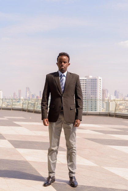 Ritratto integrale dell'uomo d'affari africano che indossa giacca e cravatta all'aperto in città mentre è in piedi