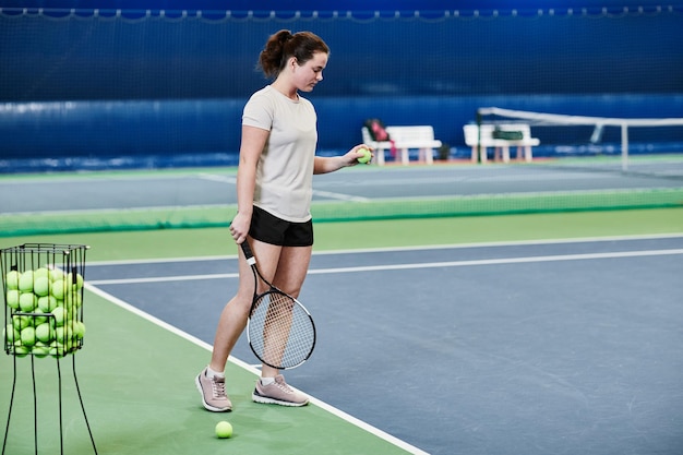 Ritratto integrale della giovane donna caucasica che gioca a tennis nello spazio della copia della corte interna