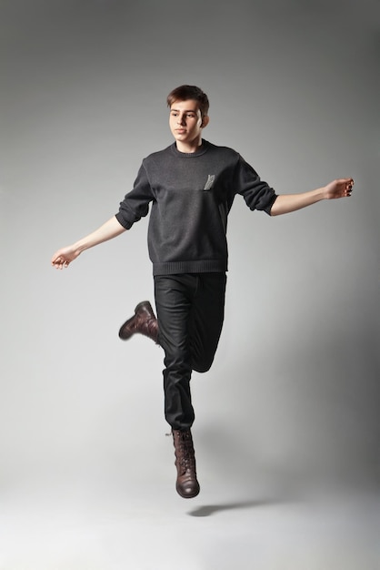 Ritratto integrale di un giovane maschio di moda che salta su sfondo grigio