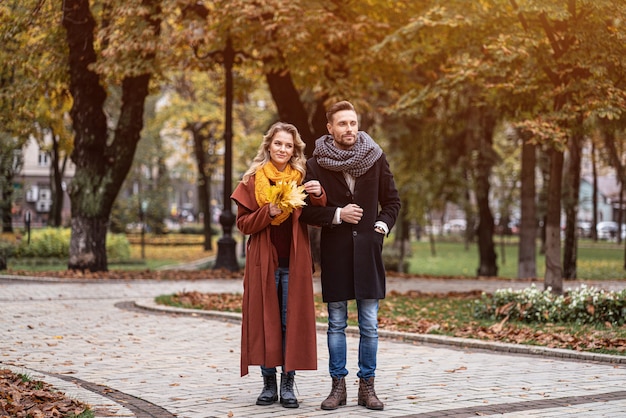 Ritratto integrale di una coppia in una data che cammina nel parco autunnale tenendosi per mano